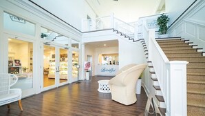 A spacious interior with a wooden floor, white furniture, a staircase, and a sign for 'Beach Club'.