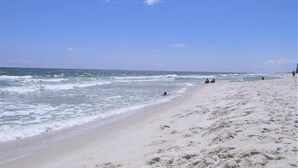 A sandy beach with footprints leading to the water, a clear sky, and a few people in the distance.