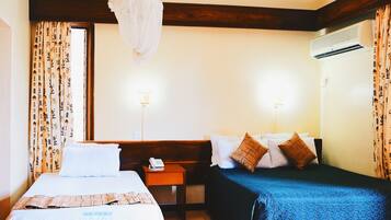 A hotel room with two beds, a wooden headboard, a bedside table with a phone, and an air conditioning unit.
