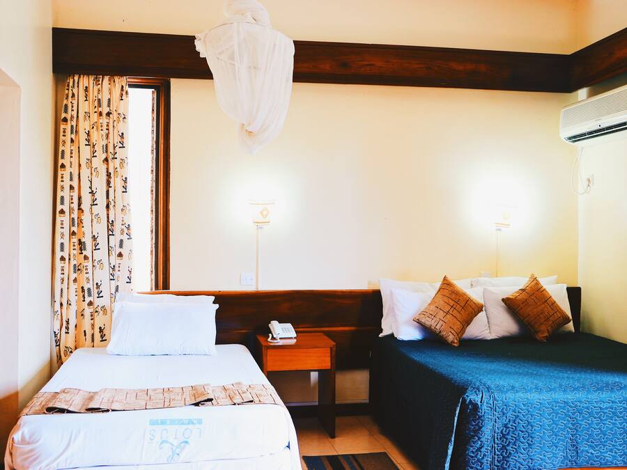 A hotel room with two beds, a wooden headboard, a bedside table with a phone, and an air conditioning unit.
