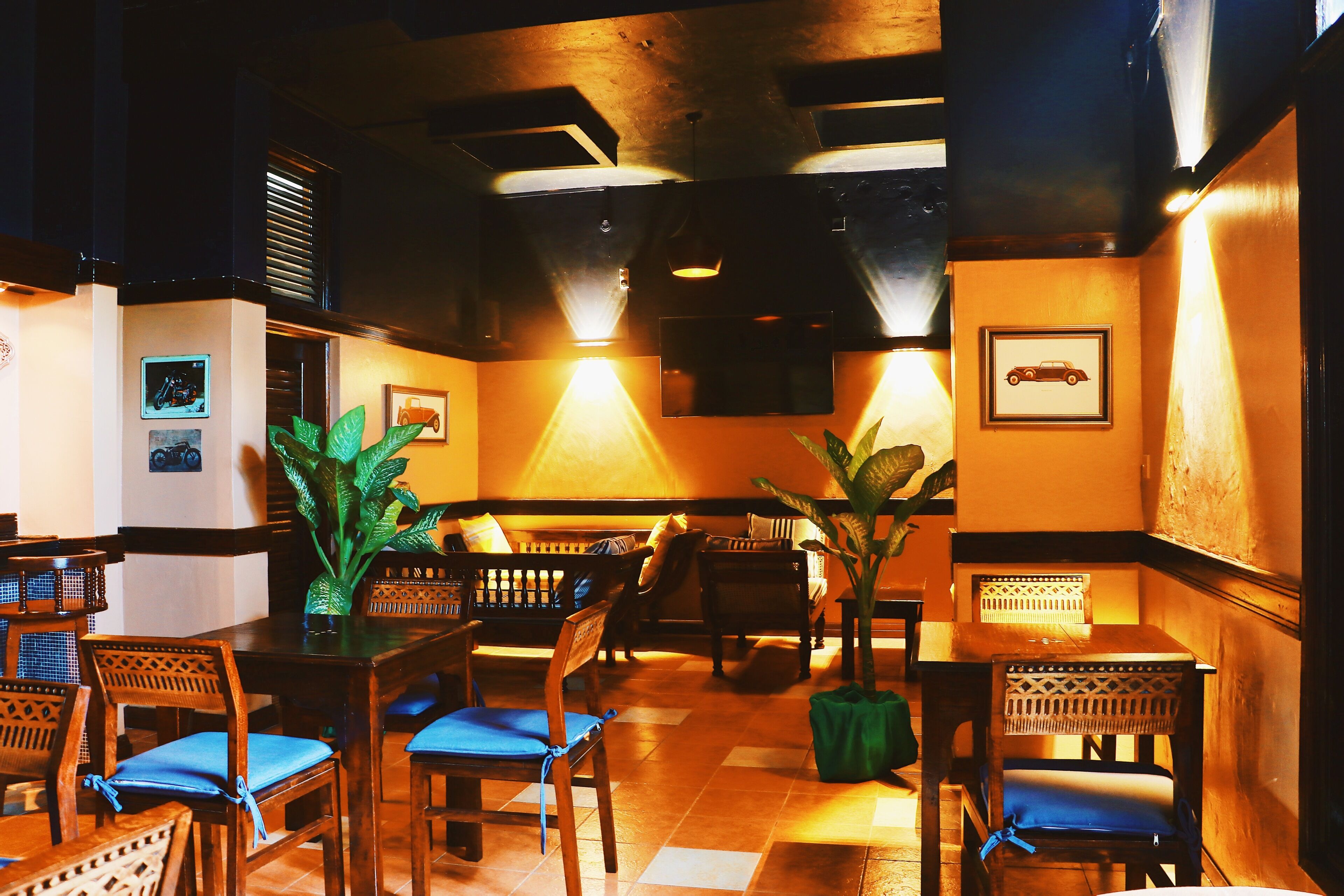 Interior de un restaurante con mobiliario de madera, plantas en macetas y cuadros en las paredes.