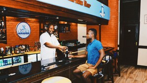 A bar area with a wooden counter, a sign for 'Lotus Hotel', and a person serving another person. - Lotus Hotel (Mombasa)