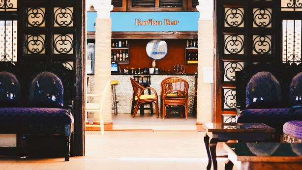 A bar area with a sign reading "Kabu Bar," featuring a wooden counter, bar stools, and a chandelier. - Lotus Hotel (Mombasa)