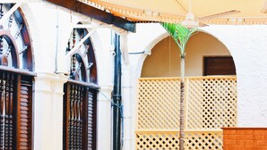 An outdoor dining area with wicker chairs and tables, a white building with arched windows, and a wooden fence. - Lotus Hotel (Mombasa)