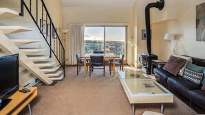 Una sala de estar con una escalera, una mesa de comedor, un sofá, un televisor y una chimenea.