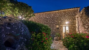 A stone building with a tiled roof, a door with glass panels, and a small garden with flowering plants. - Askos Villa (Zakynthos)
