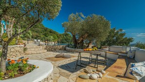 A stone patio with a pool, outdoor seating, and a table with fruits. - Askos Villa (Zakynthos)