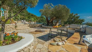 A stone patio with a pool, outdoor seating, and a table with fruits.