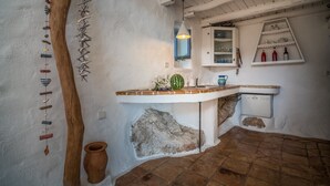 A rustic kitchen with a wooden tree trunk, a hanging wind chime, a terracotta pot, and a white cabinet with shelves. - Askos Villa (Zakynthos)