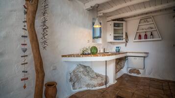 Una cocina rústica con un tronco de árbol de madera, un móvil de viento colgante, una maceta de terracota y un armario blanco con estantes.