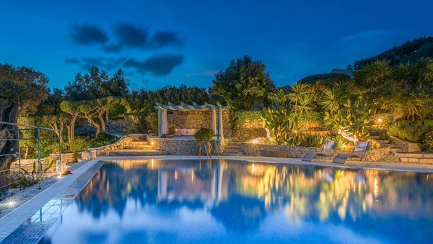 A serene pool area with a stone wall, a pergola, and lounge chairs. - Askos Villa (Zakynthos)