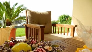 Una terraza de madera con una silla acolchada y una mesa decorada con flores y un frutero.
