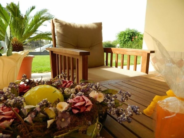Una terraza de madera con una silla acolchada y una mesa decorada con flores y un frutero.