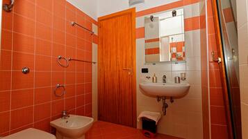A bathroom with orange tiles, a wooden door, a sink, a toilet, and a shower area.