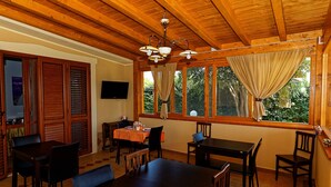 Un comedor con mesas y sillas de madera, una araña y ventanas grandes con cortinas.