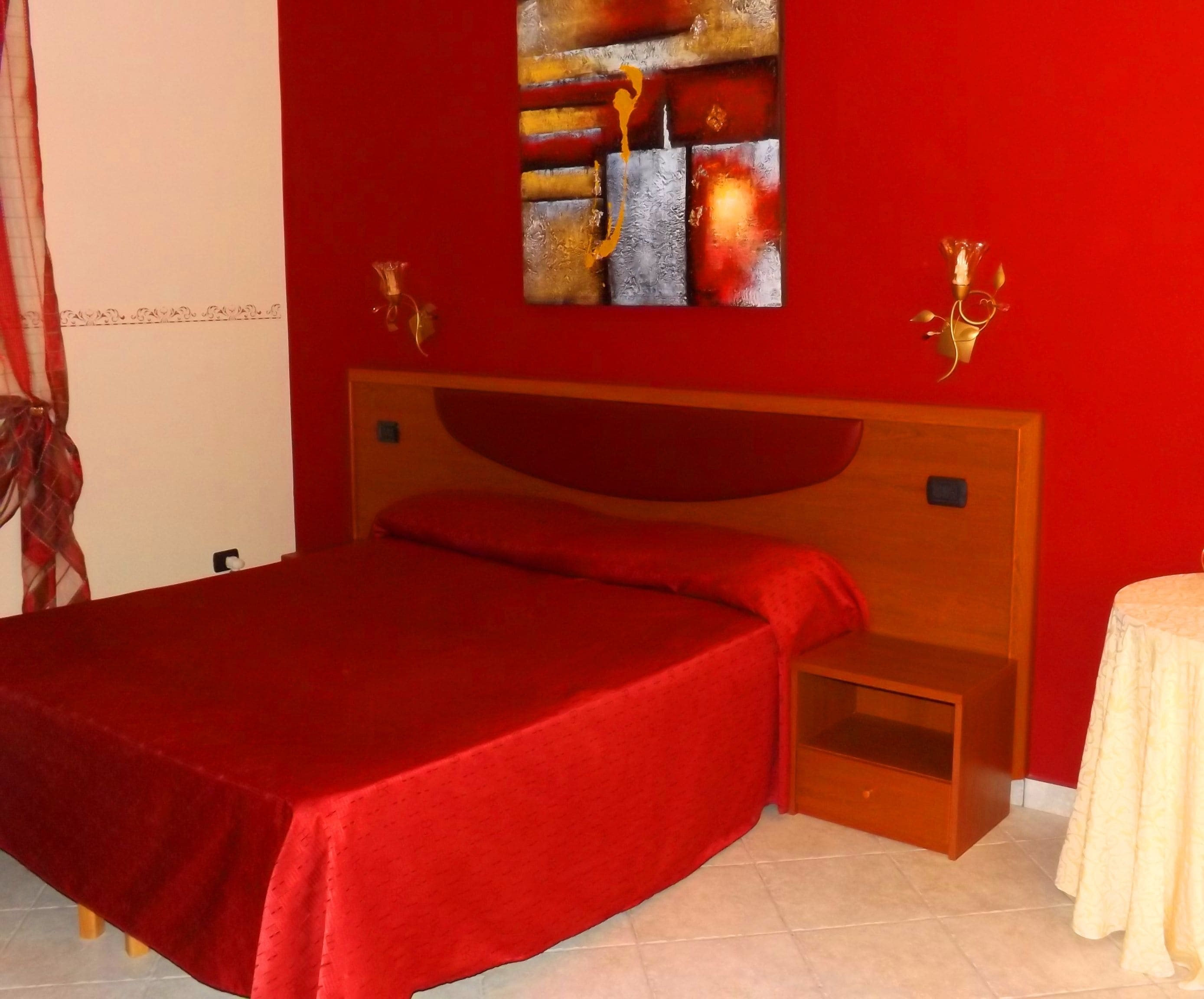 A bed with a red bedspread, a wooden headboard, and a small bedside table with a lamp.