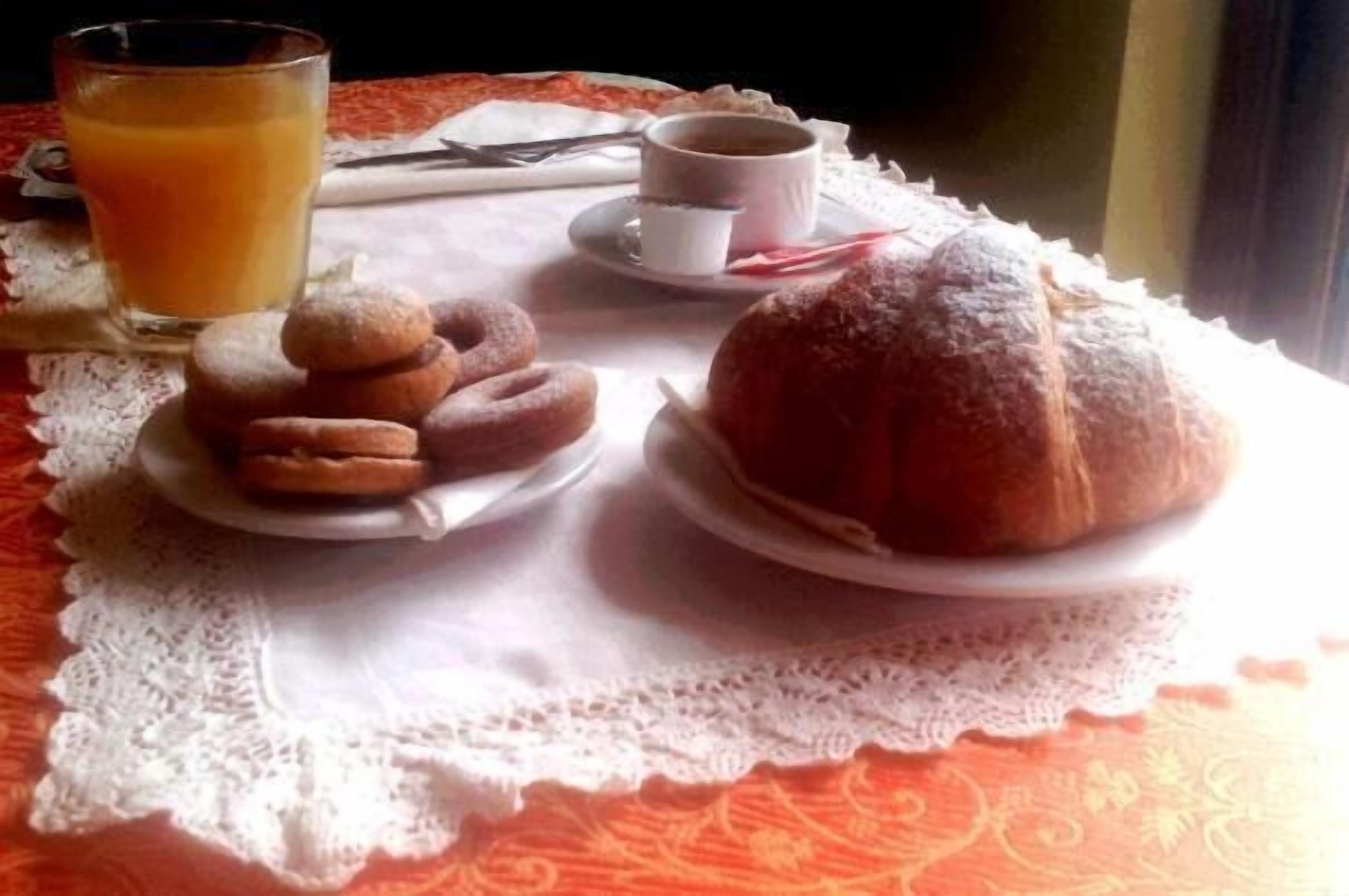A breakfast setting with pastries, a glass of orange juice, and a cup of coffee on a lace tablecloth.