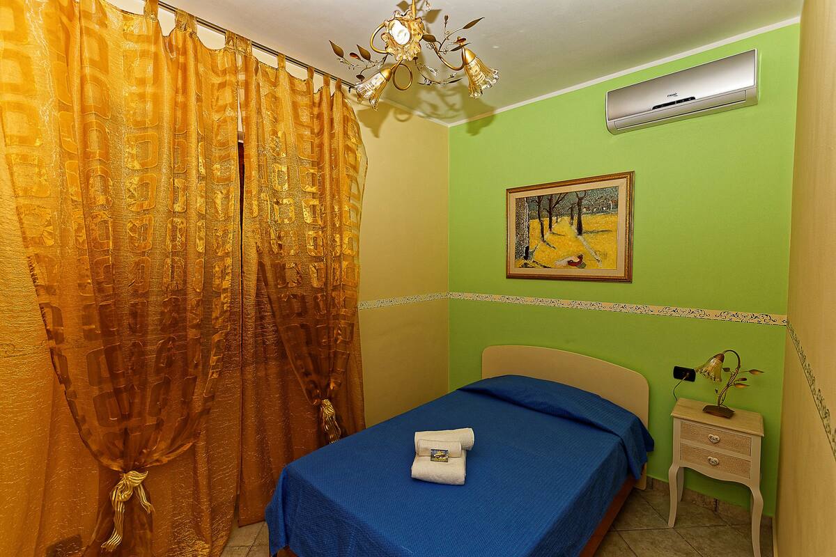 A room with a bed, a nightstand, an air conditioner, a painting, and a chandelier.