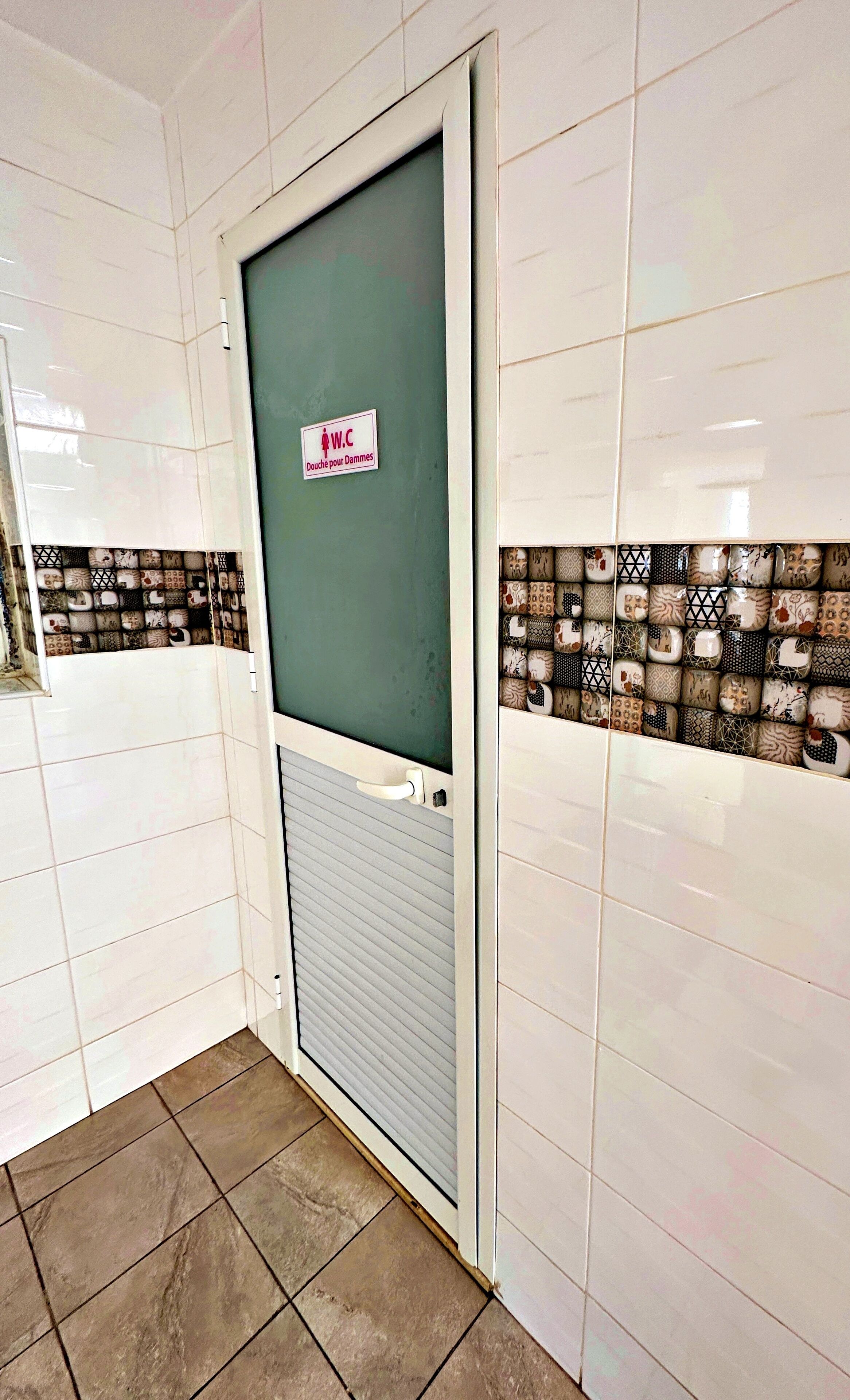 A restroom with a tiled wall, a sign indicating a women's toilet, and a patterned tile backsplash.