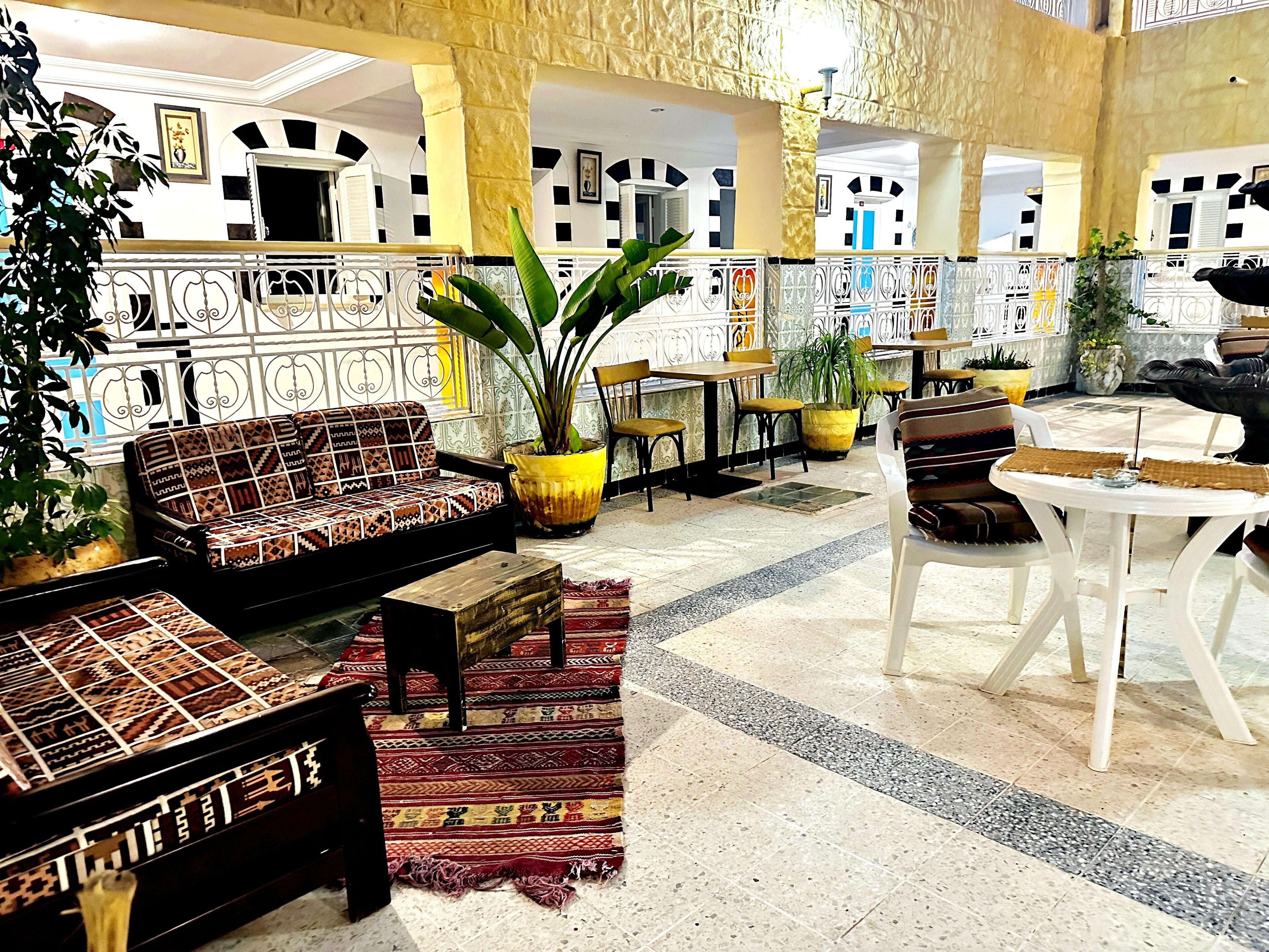 A spacious lobby with a patterned sofa, a dining area with tables and chairs, and decorative plants.