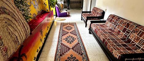 Un pasillo con un sofá, dos sillones, un tapete estampado y un detalle decorativo en la pared.