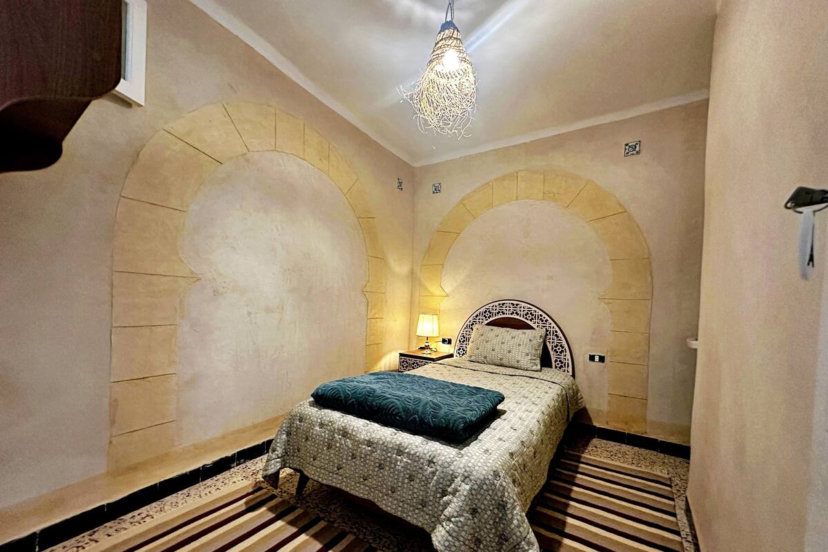 A room with a bed, a nightstand, a lamp, and a decorative ceiling light.