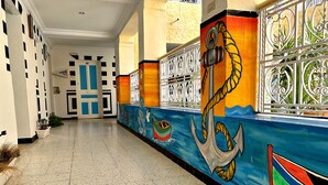 A hallway with a mural of an anchor, a door with a blue frame, and a window with decorative metal bars.