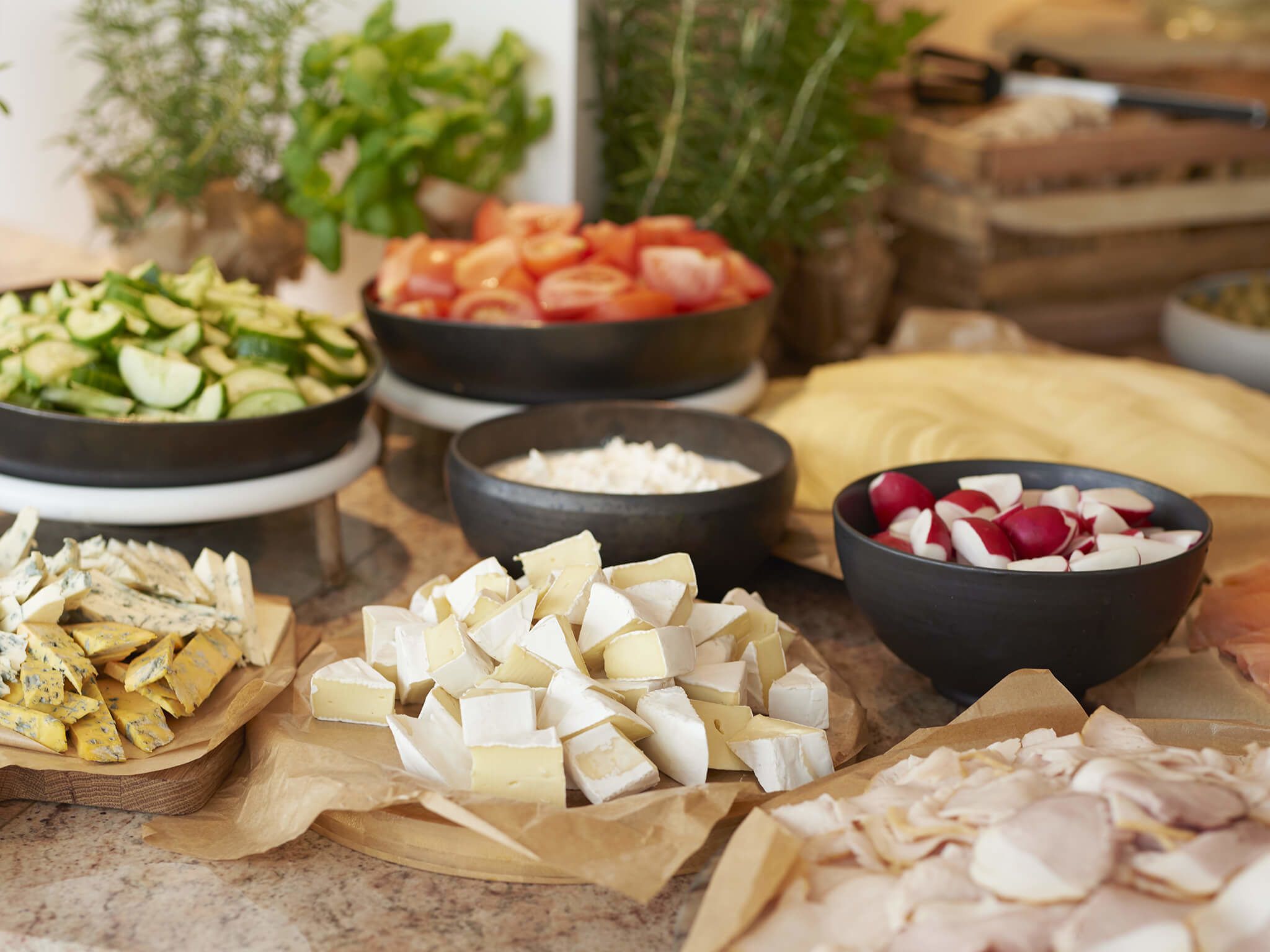 Variedad de alimentos como queso, tomates, pepinos, rábanos y almendras sobre una encimera de cocina.