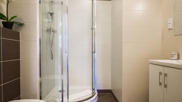 A modern bathroom with a glass-enclosed shower, white tiles, and a small potted orchid.