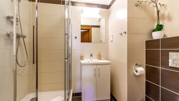 A modern bathroom with a glass shower enclosure, a sink with a mirror above, and a potted orchid on the wall.