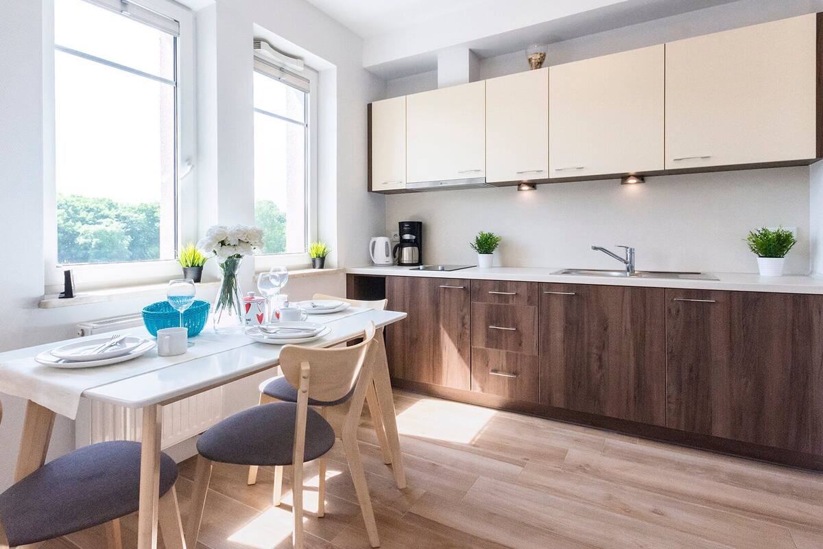 A modern kitchen with wooden cabinets, a white countertop, and a dining area with a table set for two.