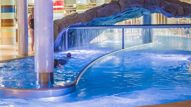 An indoor water slide with a rocky backdrop, a pool, and a person in a swimsuit. - VacationClub - Aquamarina Apartments (Swinoujscie)