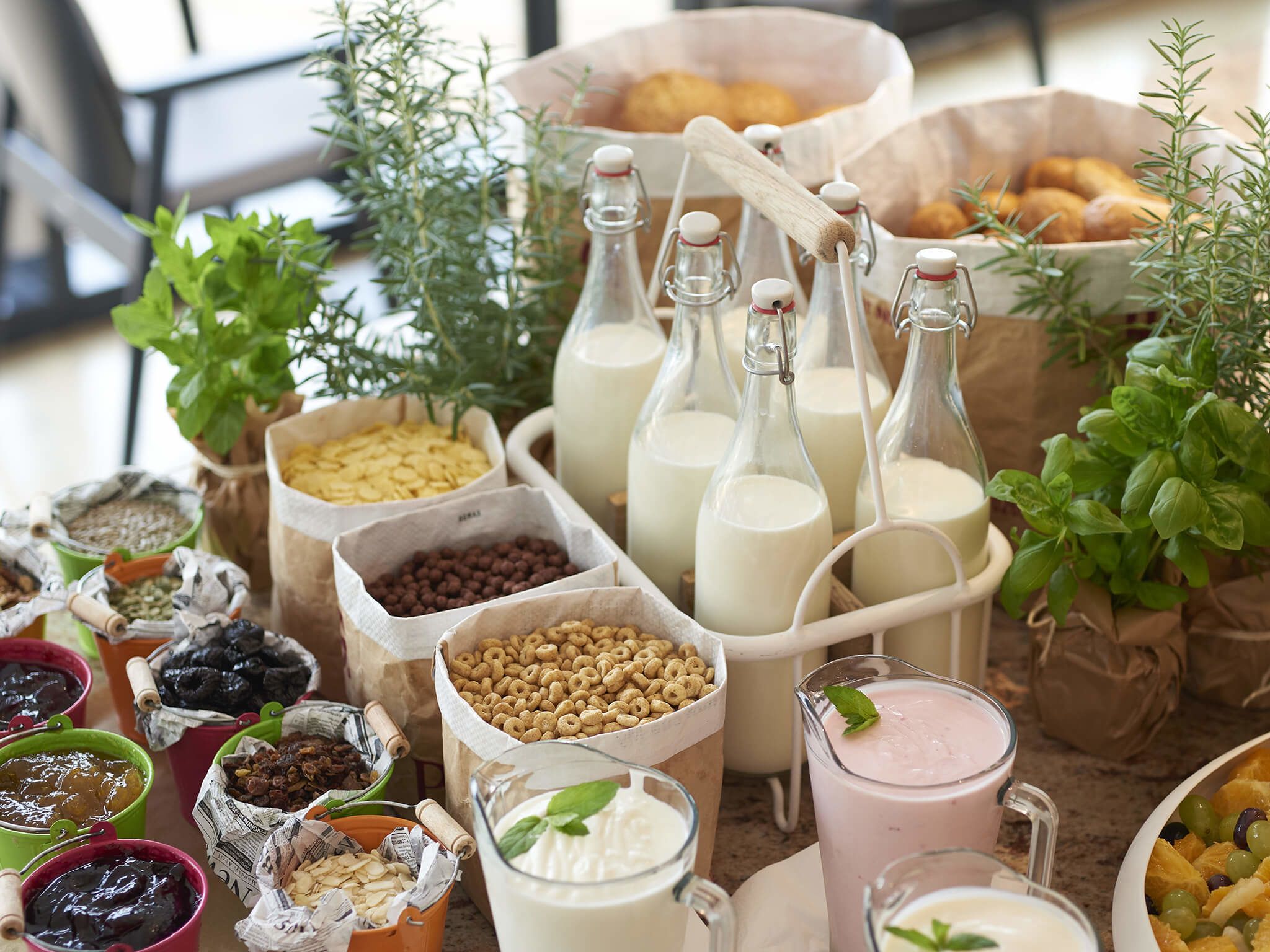 Variedad de alimentos y bebidas, incluyendo frascos de conservas, cereales y botellas de leche, dispuestas sobre una mesa.