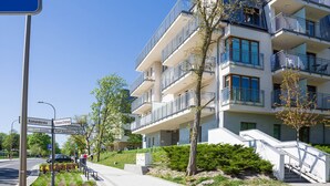 A multi-story residential building with balconies, a clear sky, and a street sign indicating directions to various locations. - VacationClub - Aquamarina Apartments (Swinoujscie)