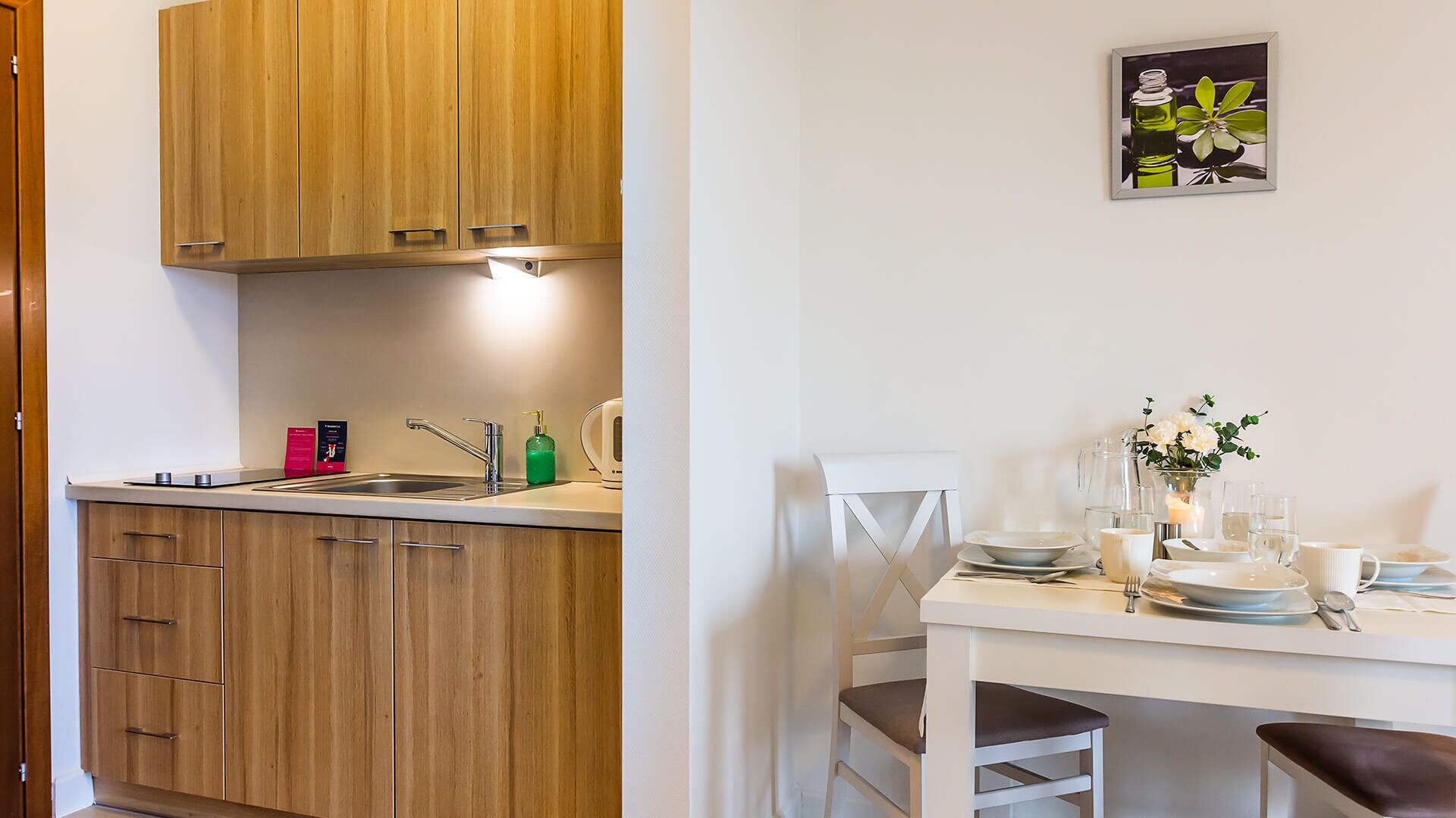 A compact kitchen with wooden cabinets, a white countertop, and a dining area with a white table and chairs.