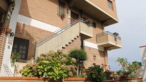 Een meerlaags gebouw met een bakstenen gevel, een centrale trap en balkons met plantenbakken.
