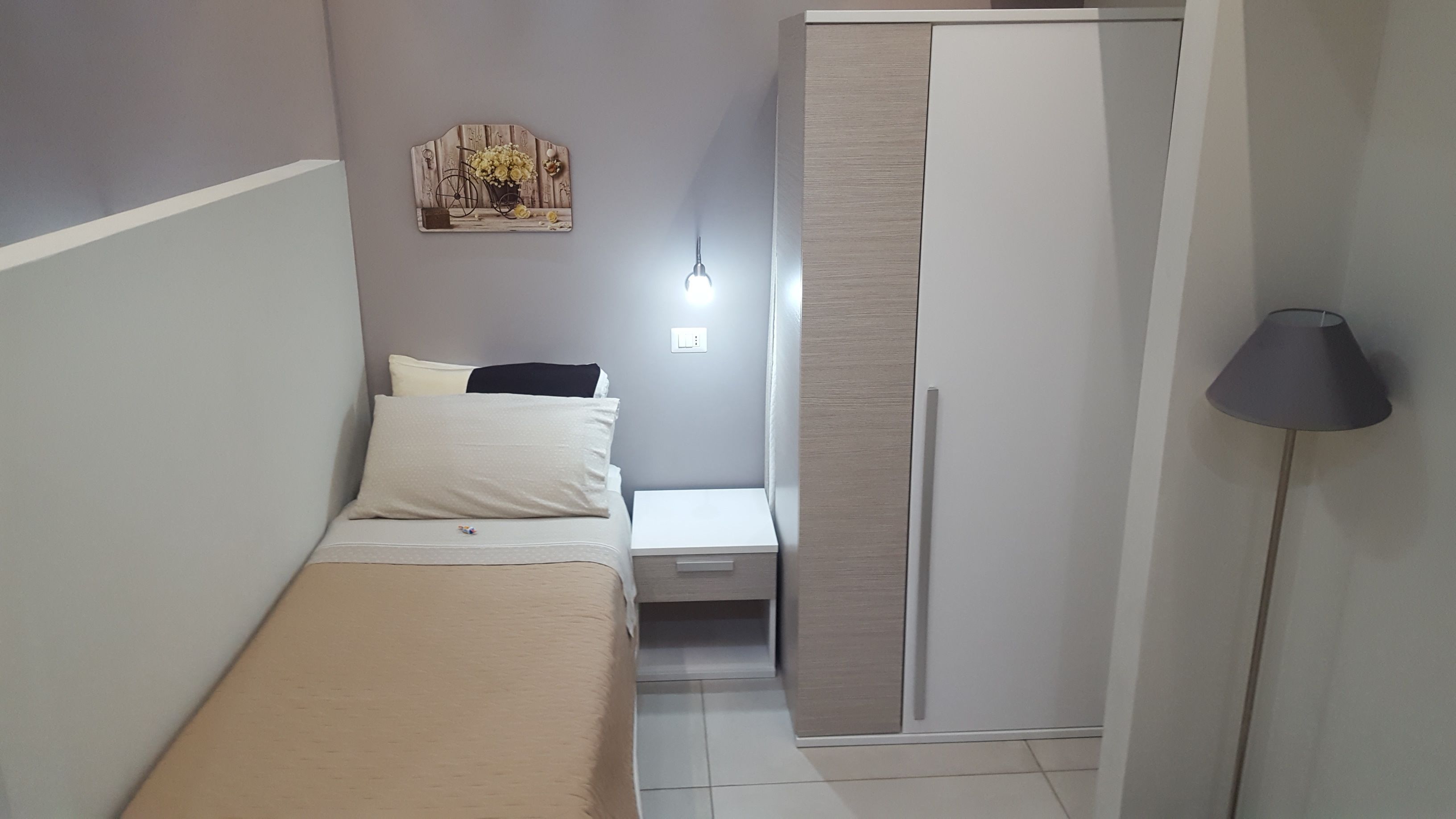 Ein Schlafzimmer mit Bett, Nachttisch, Kleiderschrank und einem an der Wand befestigten Regal mit Blumen und einem Fahrrad.