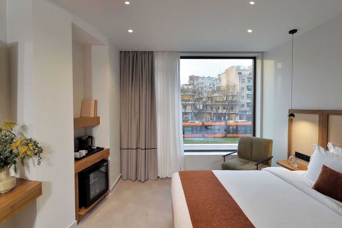 Habitació d'hotel amb un llit, una cadira, escriptori amb una màquina de cafè, televisió i finestra amb vista a la ciutat.