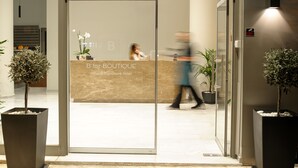 Entrada d'hotel amb una recepció, plantes en testos i un cartell que diu "B for BOUTIQUE athena signature hotel".