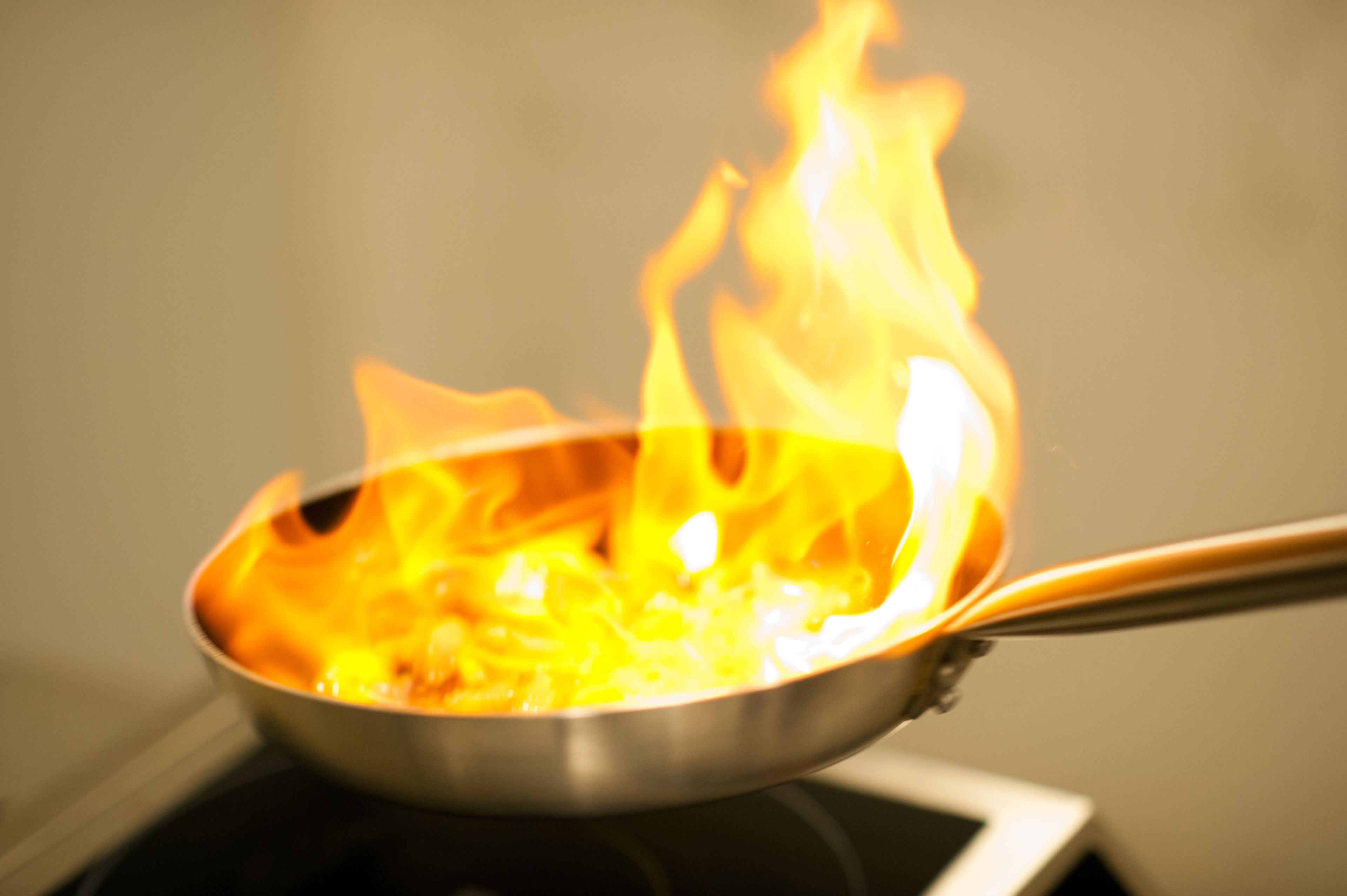 Une poêle sur une cuisinière, avec des flammes.