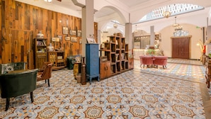Una habitación amplia con suelo estampado, paneles de madera y una variedad de muebles, incluyendo un aparador azul, un sillón rojo y una estantería de madera.