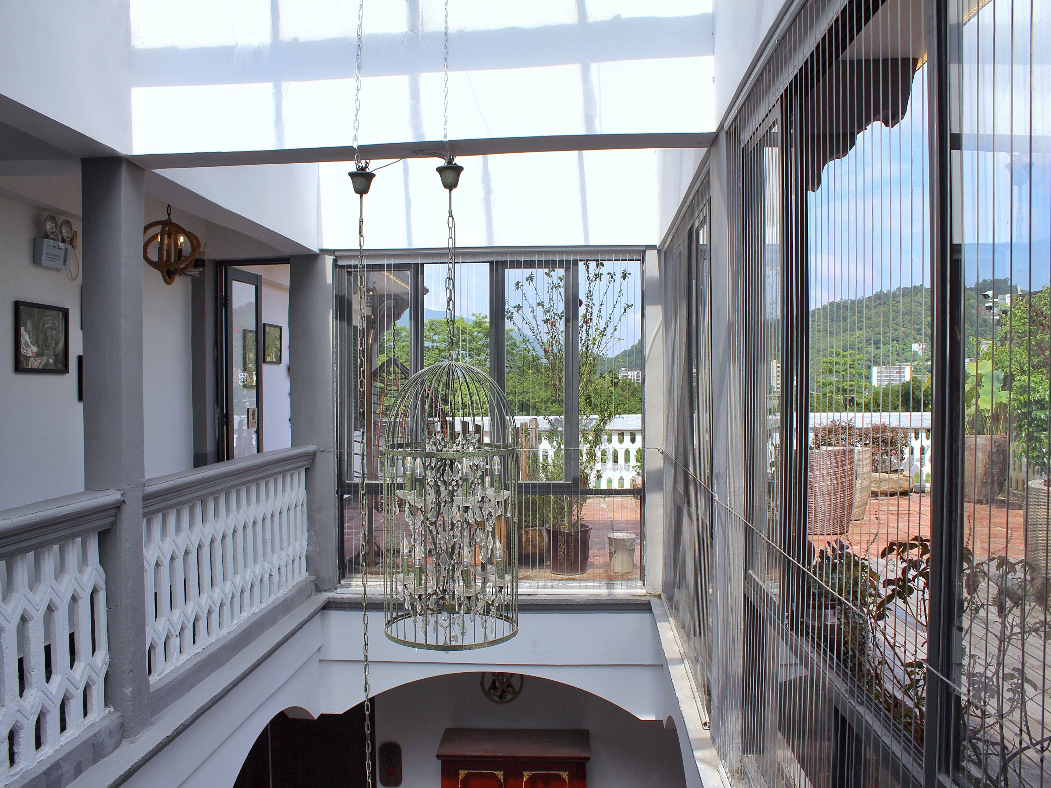 A spacious balcony with a wrought iron railing, a hanging chandelier, and a view of a lush green hillside.