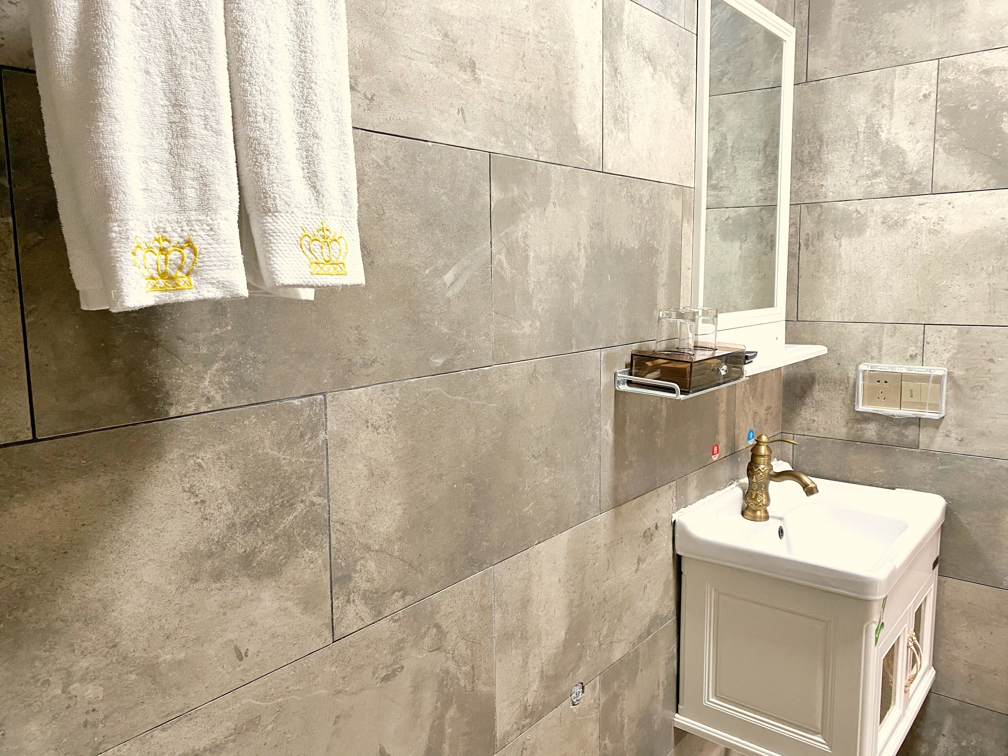 A bathroom with a white sink, a mirror, and two towels with a crown emblem.
