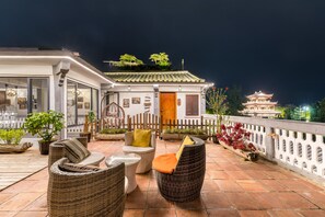 Una terraza en la azotea con mobiliario de mimbre, un edificio tradicional con techo de tejas y una pagoda al fondo.