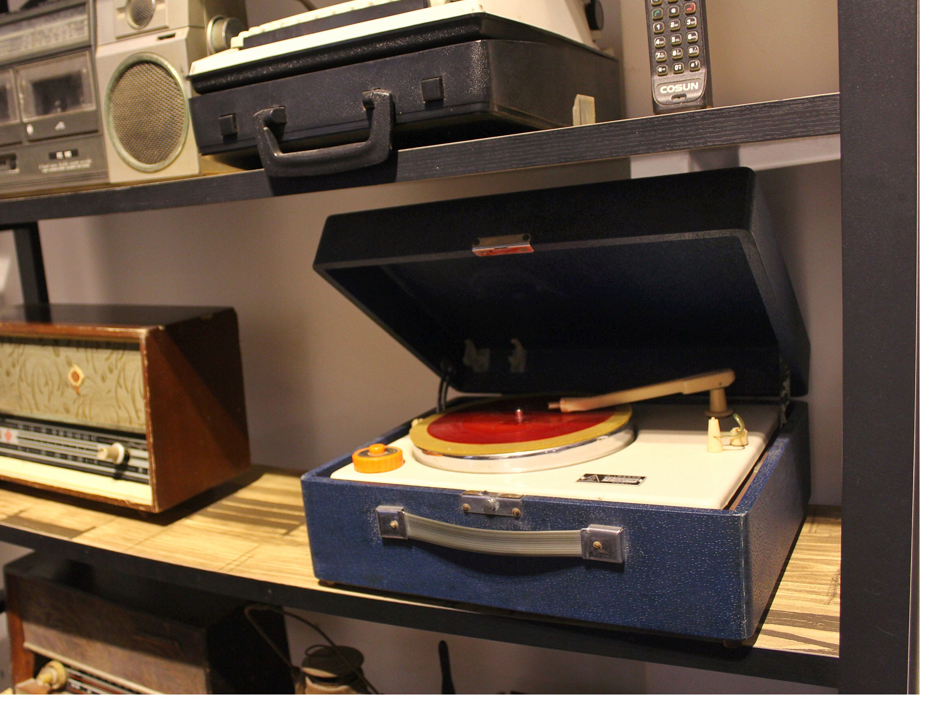 A vintage record player on a shelf with a radio and a cassette player.