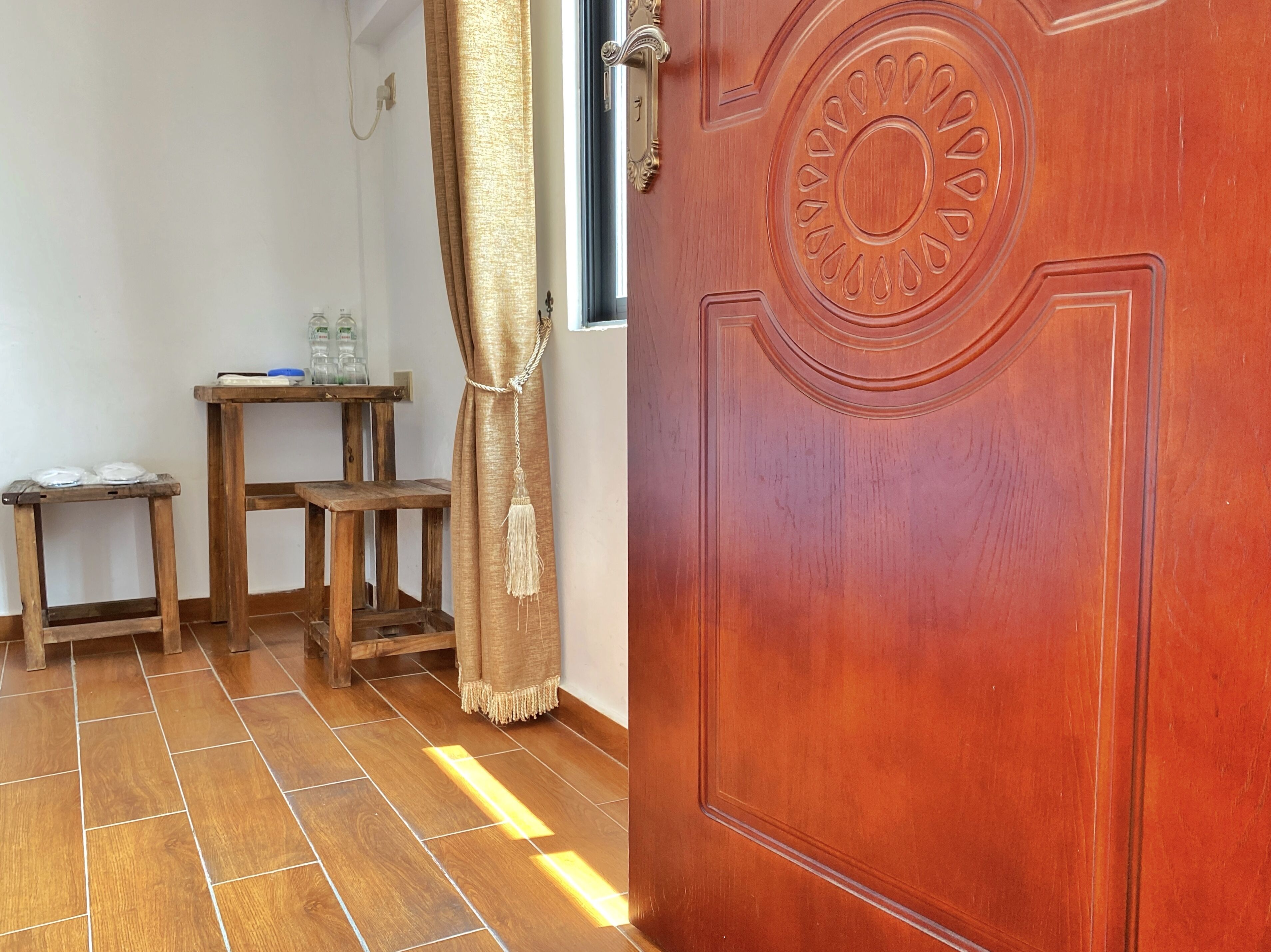Une porte en bois ornée d’un motif circulaire, un banc en bois, une petite table sur laquelle sont posés divers objets, et un rideau.