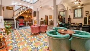 Un vestíbulo amplio con un suelo de estampado llamativo, una escalera y diversas opciones de asiento, incluyendo sillones tapizados de verde y una silla de ruedas roja.