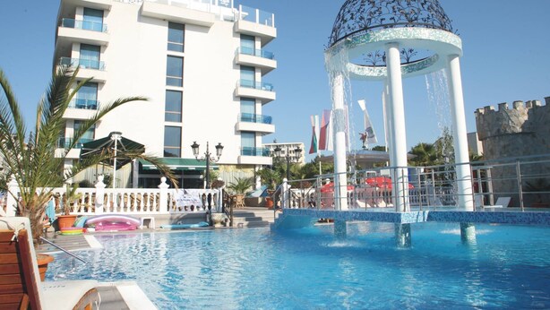 A hotel pool area with a decorative fountain, a modern building with balconies, and a clear blue sky. - Kiten Beach (Kiten)
