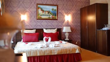 A hotel room with a bed, red pillows, a painting on the wall, and a wardrobe.