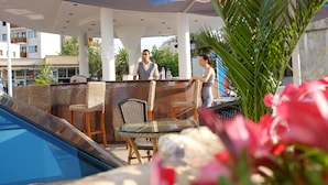 A poolside bar area with wicker furniture and a glass table, surrounded by a pool and a decorative umbrella. - Kiten Beach (Kiten)